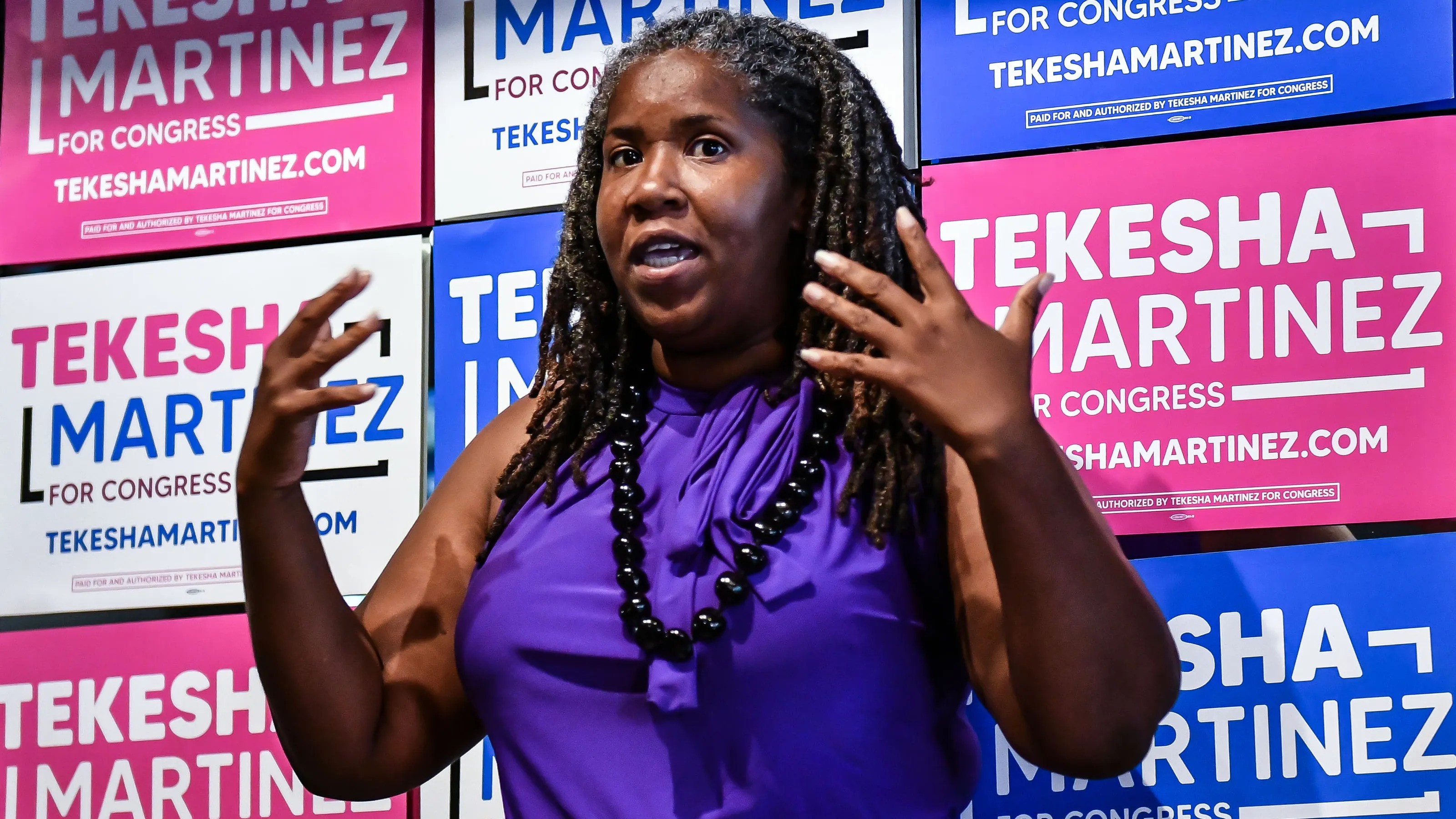 Tekesha Martinez standing in front of colorful pink and blue Tekesha Martinez for Congress signs